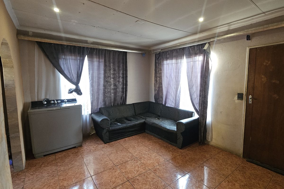 A living area featuring tiled flooring and recessed ceiling lighting, requiring cosmetic updates to the walls and ceiling to improve the overall aesthetic.