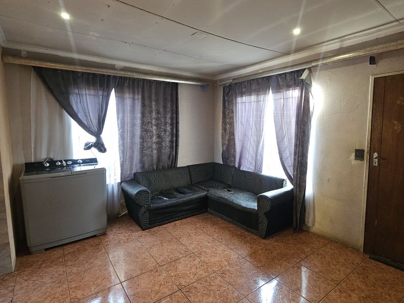 A living area featuring tiled flooring and recessed ceiling lighting, requiring cosmetic updates to the walls and ceiling to improve the overall aesthetic.