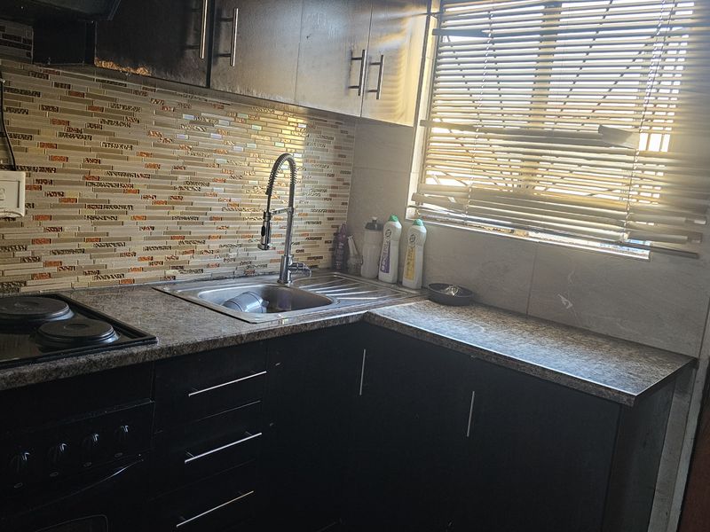 Compact kitchen featuring dark cabinetry, granite countertops, a mosaic tile backsplash, and a built-in electric hob.