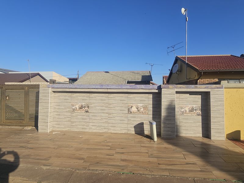 Front exterior view featuring a tiled boundary wall, paved driveway, and metal sliding gate entrance.