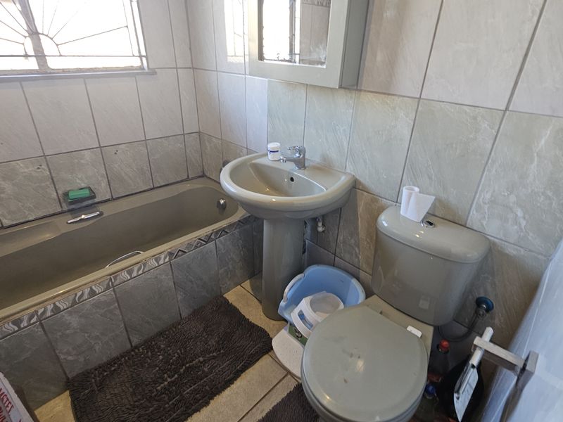 A functional bathroom featuring a pedestal basin, bathtub, and toilet with neutral wall and floor tiling, requiring cosmetic updates to modernize the space.