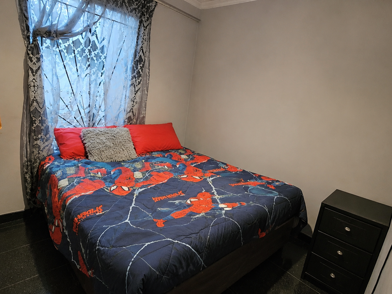 A compact bedroom featuring tiled flooring and a window fitted with security bars.