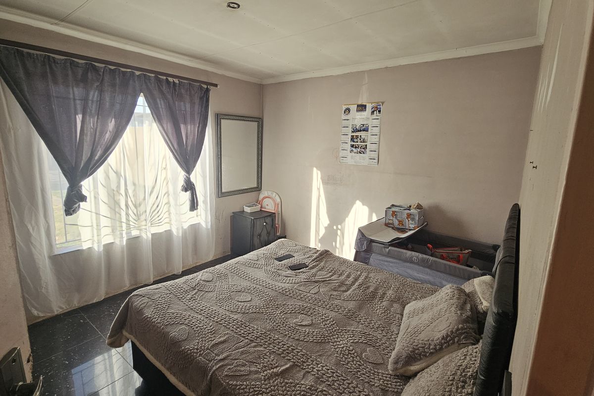 A bedroom featuring dark tiled flooring and a window with security bars, requiring cosmetic updates to the walls and ceiling.