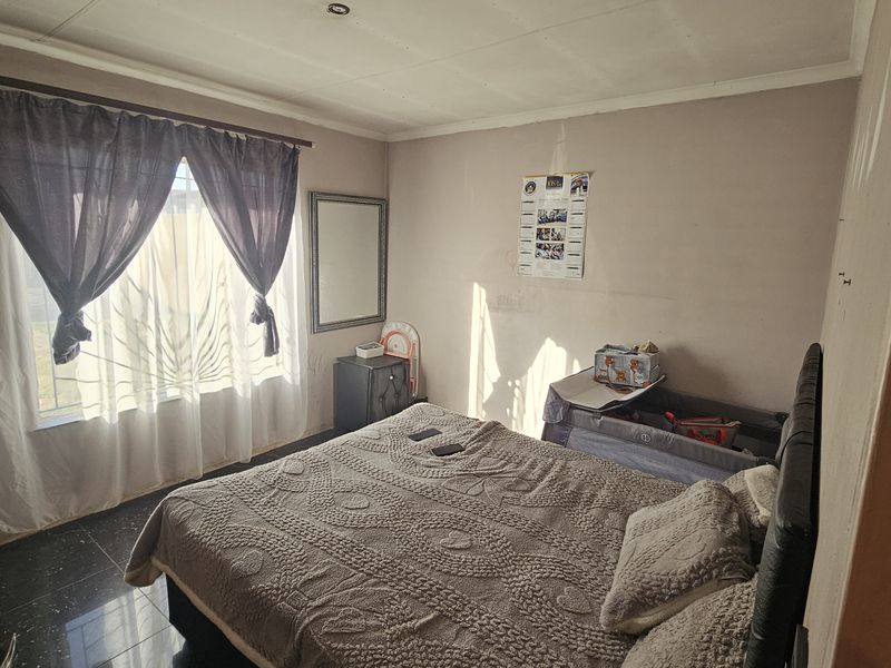 A bedroom featuring dark tiled flooring and a window with security bars, requiring cosmetic updates to the walls and ceiling.