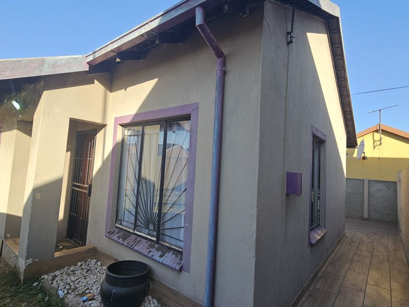 Front elevation of a residential house featuring security bars, tiled side walkway, and exterior wall finishes requiring maintenance.