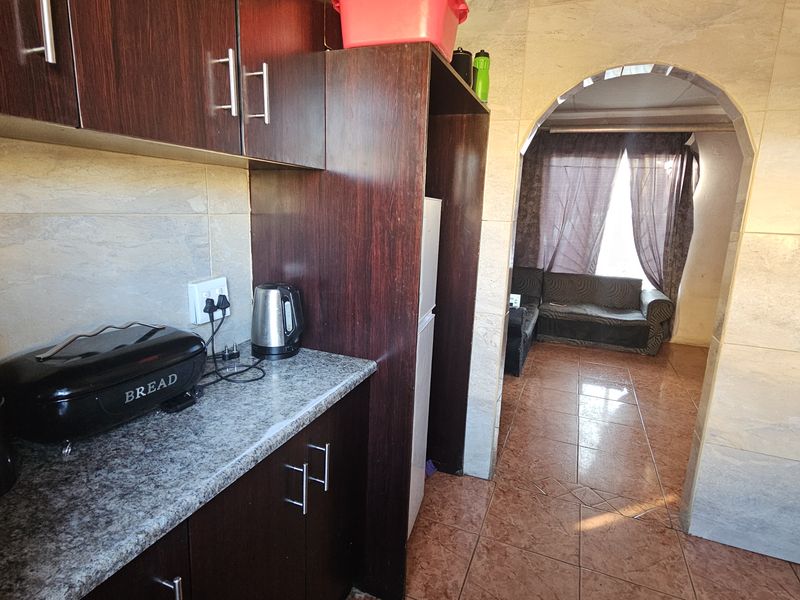 A compact kitchen featuring dark wood cabinetry, granite-look countertops, and tiled finishes, leading through an arched doorway into the adjacent living area.