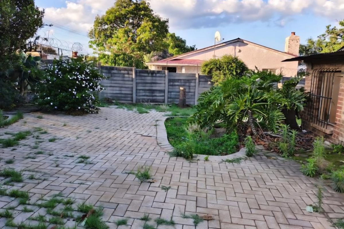 Rear garden area featuring a paved patio, perimeter precast concrete walling, and established garden beds requiring maintenance.