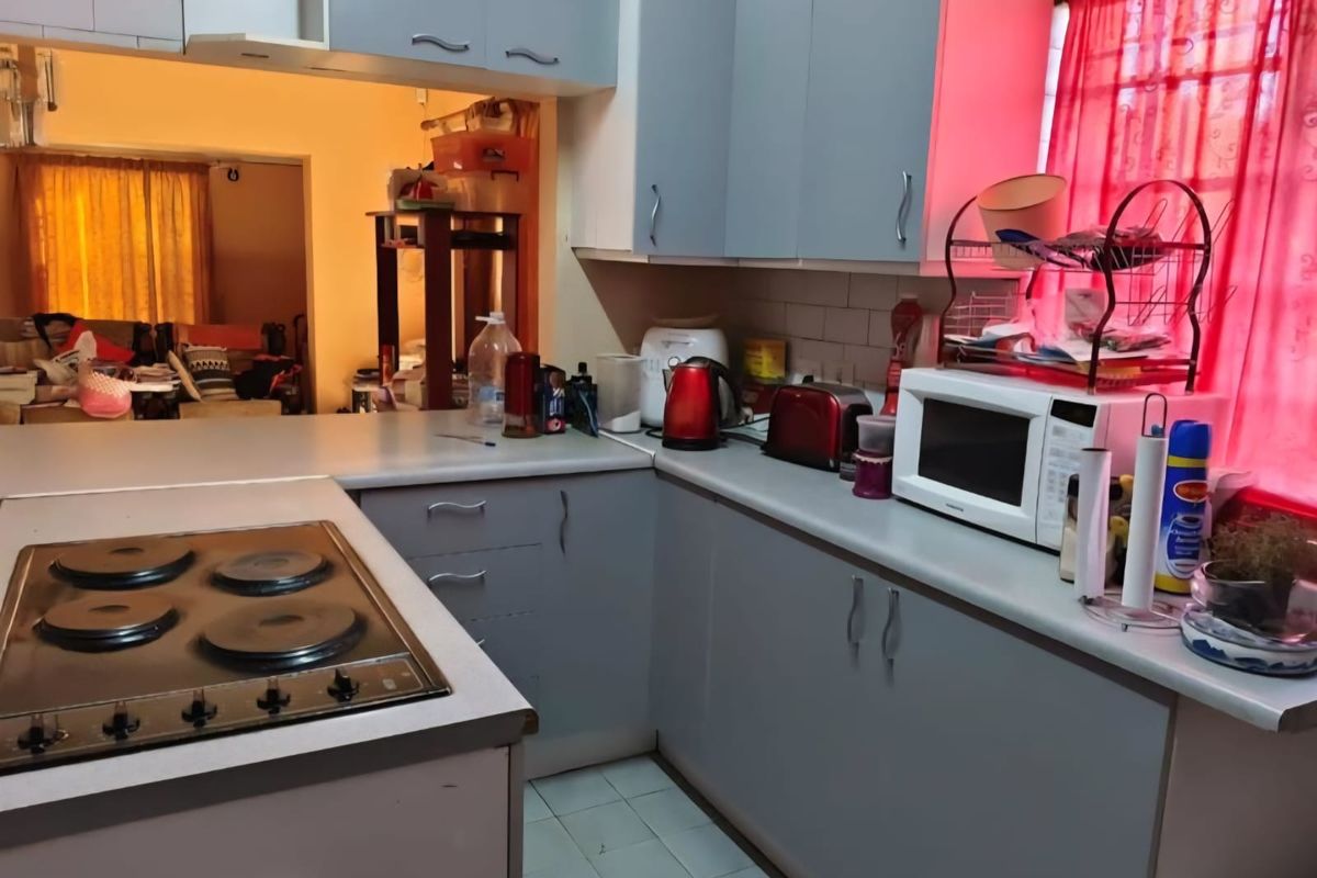 A functional kitchen featuring built-in cabinetry, laminate countertops, and an integrated electric hob, with a view into the adjacent living area.