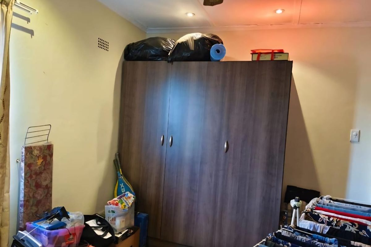 A bedroom featuring a large built-in wardrobe, ceiling fan, and recessed lighting, currently used for storage.
