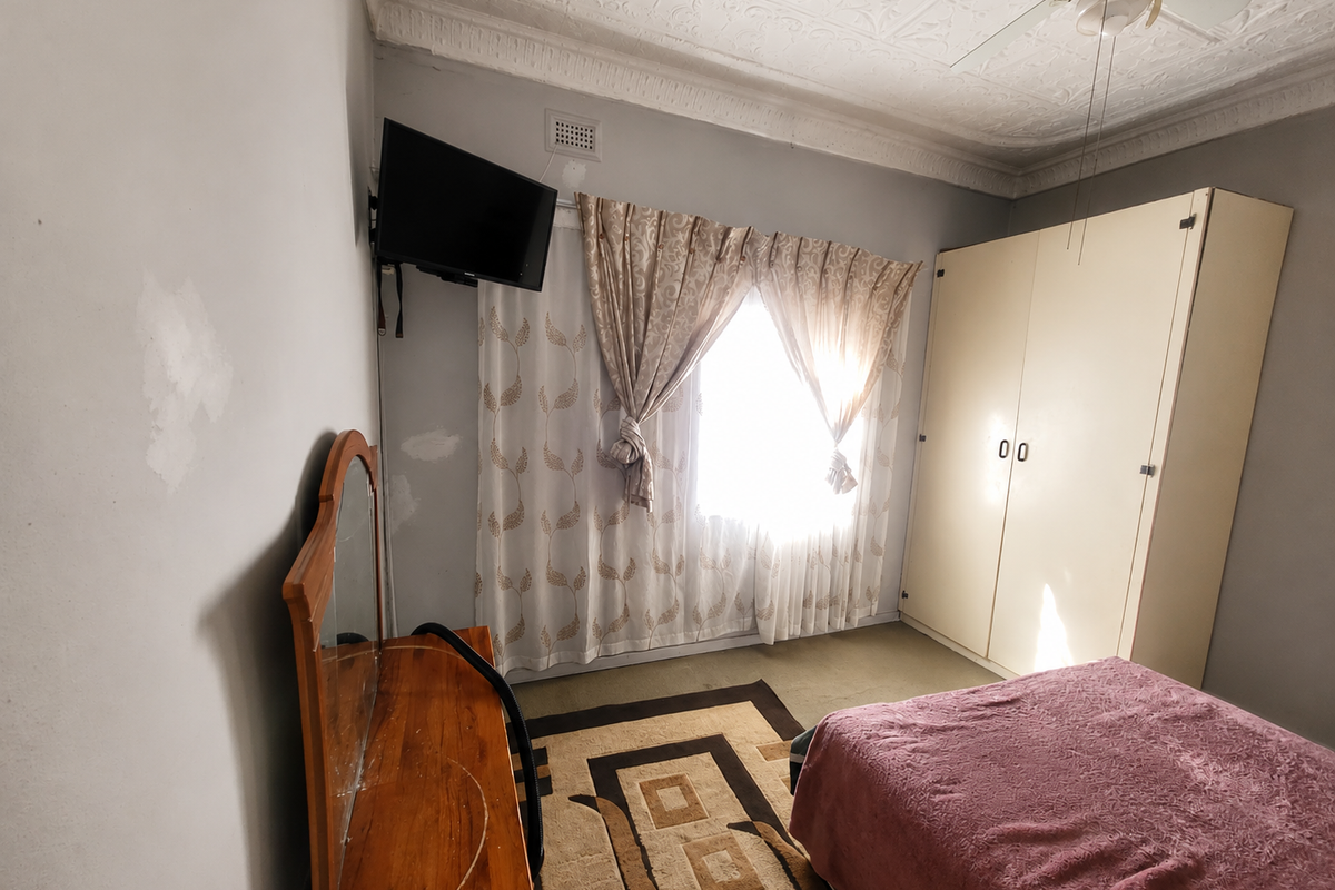 A bedroom featuring a built-in wardrobe, decorative ceiling detailing, and a ceiling fan. The walls require cosmetic attention and repainting.