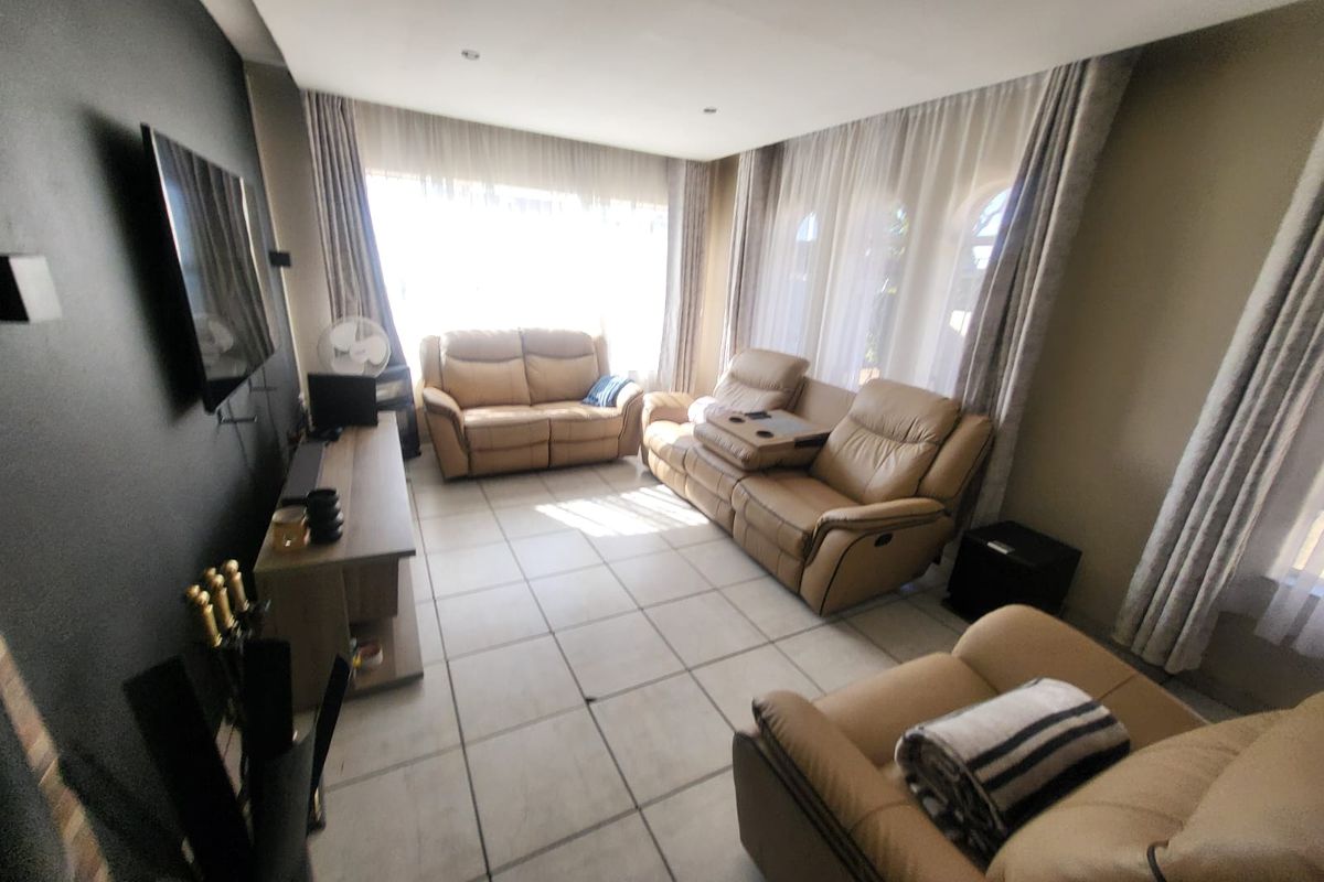 A spacious living room featuring large windows with curtains, tiled flooring, and recessed downlighting, providing a comfortable and bright area for relaxation.