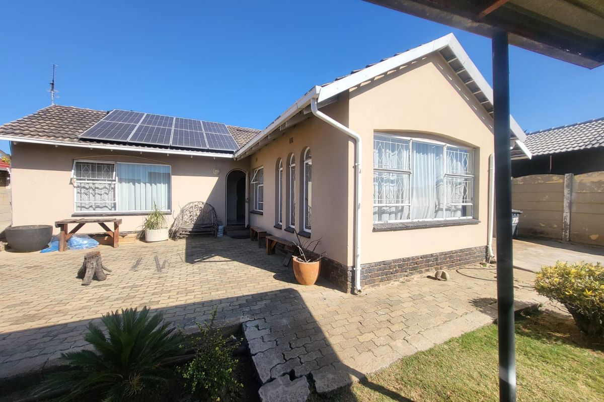 Rear view of the house featuring a paved patio area, solar panels on the roof, and security bars on the windows.