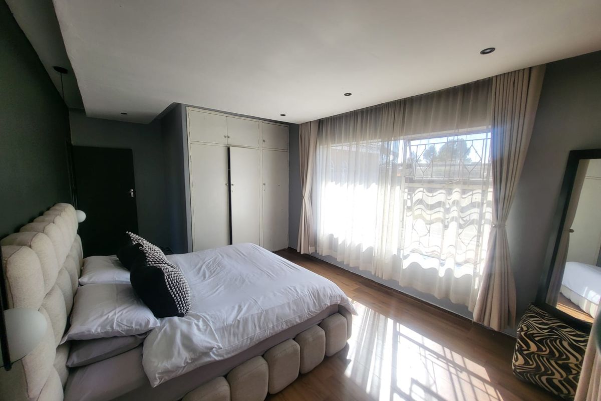 A well-lit bedroom featuring laminate flooring, built-in cupboards, and large windows with security bars, creating a comfortable and functional living space.