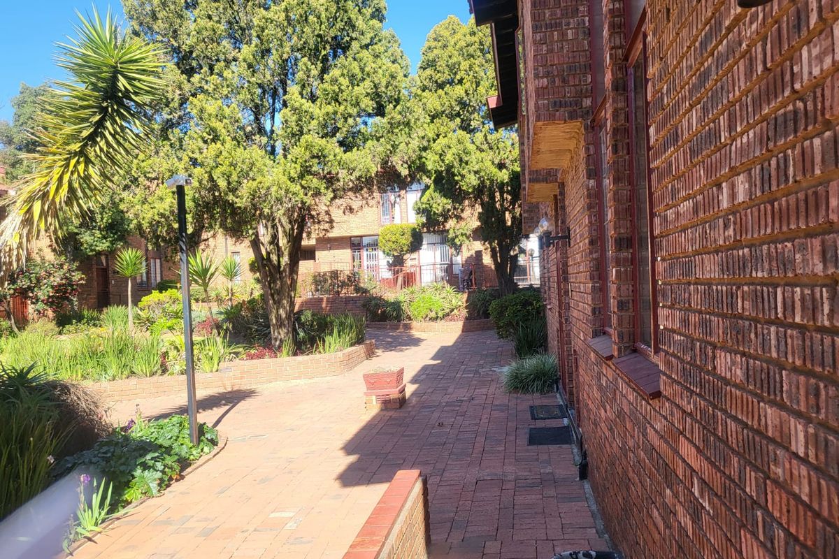 A view of the rear exterior area featuring brick paving, a brick townhouse facade, and established garden landscaping.