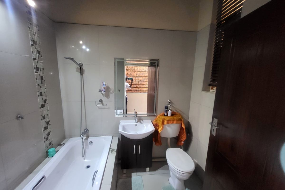 A well-maintained bathroom featuring a bathtub with shower mixer, vanity basin, toilet, and modern tiled walls with a decorative mosaic accent.