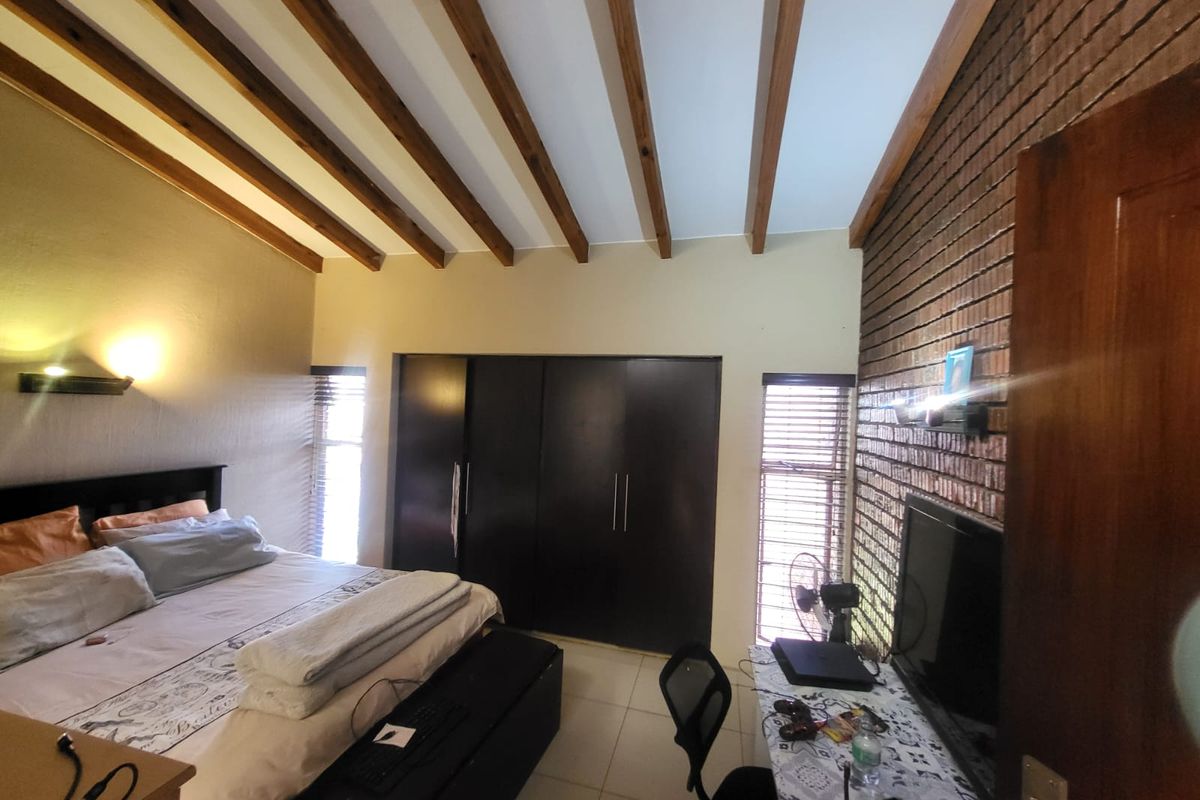 Spacious bedroom featuring exposed timber ceiling beams, a striking exposed brick feature wall, and built-in cupboards with tiled flooring throughout.