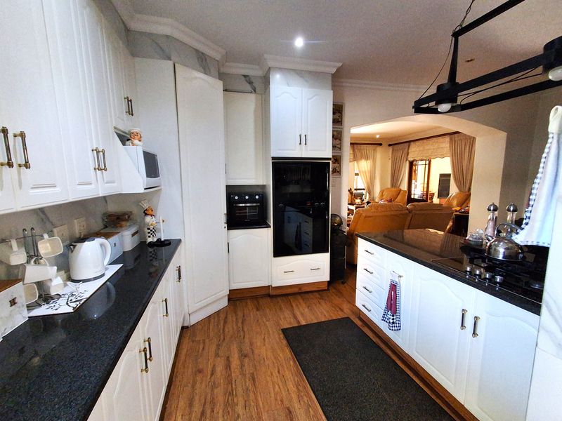 A well-maintained kitchen featuring white cabinetry, dark granite countertops, built-in appliances, and laminate flooring, with an open-plan flow into the adjacent living area.