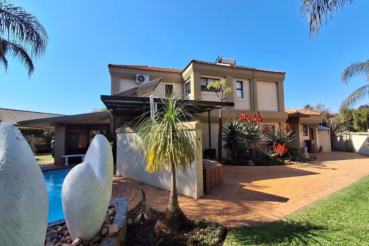 Rear exterior view of the property featuring a swimming pool, paved patio area, and established garden landscaping with a solar water heating system.