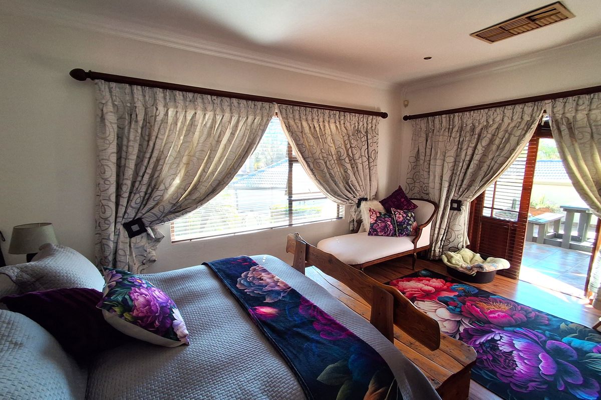 A well-lit bedroom featuring timber flooring, ducted air conditioning, and direct access to an outdoor patio area through sliding glass doors.