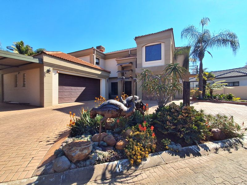 A well-maintained front elevation featuring a paved driveway, double garage, covered carport, and established landscaped garden with mature plantings.