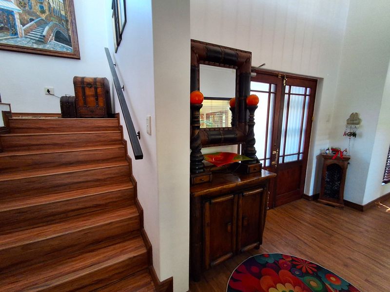 Welcoming entrance foyer featuring a timber staircase with a matching handrail and warm timber flooring, leading to a classic timber-framed glass entry door.