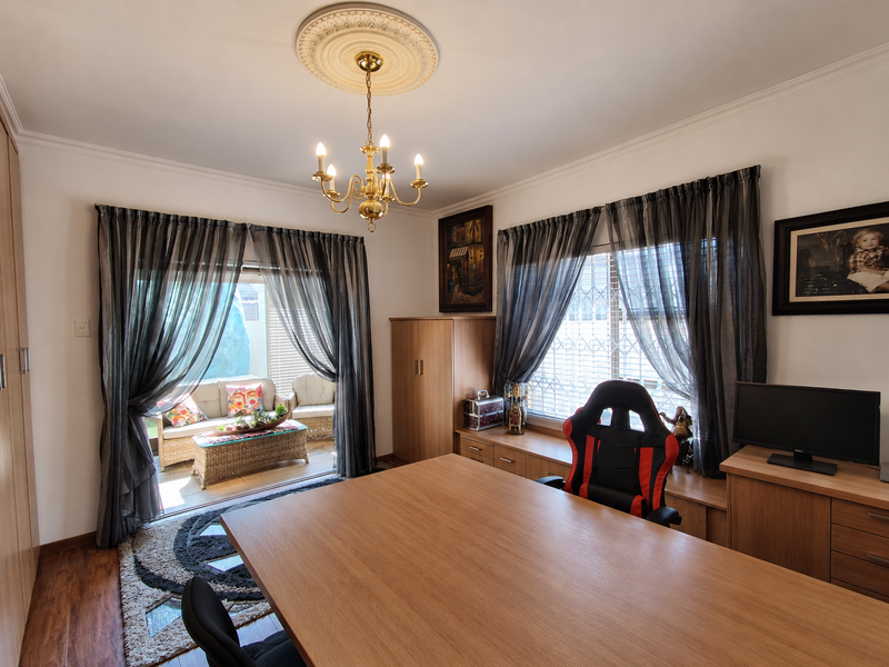 A well-maintained home office featuring built-in cabinetry, a decorative ceiling rose with a chandelier, and direct access to an outdoor patio area.