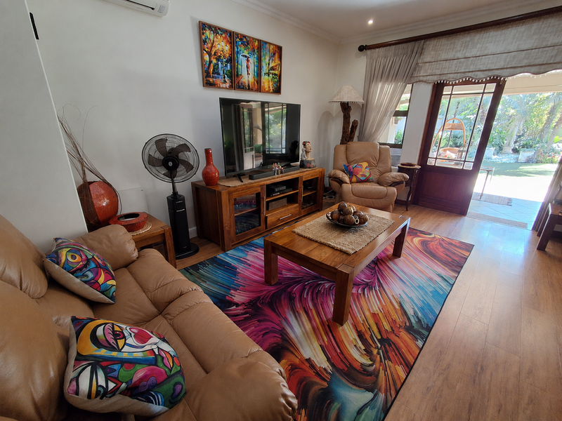 A comfortable living room featuring laminate flooring, a split-system air conditioner, and direct access to an outdoor patio area through a timber-framed glass door.