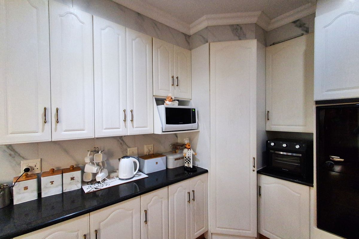 A well-maintained kitchen featuring white cabinetry, black granite countertops, and integrated appliances including an oven and microwave.