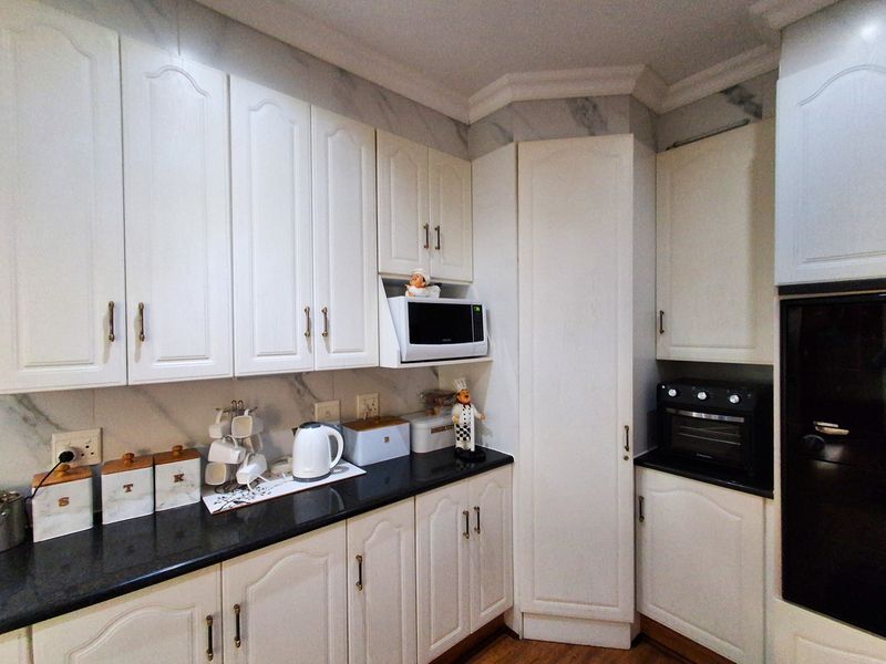 A well-maintained kitchen featuring white cabinetry, black granite countertops, and integrated appliances including an oven and microwave.