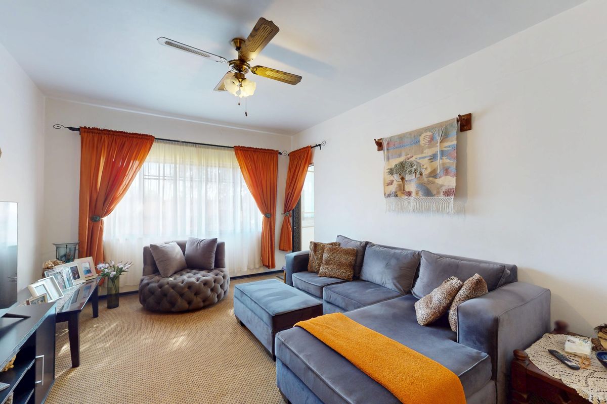 A comfortable living room featuring a ceiling fan and large windows with curtain rods, providing a bright and inviting space for relaxation.