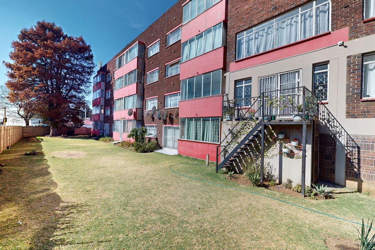 Rear view of a multi-story apartment building featuring a brick facade, metal staircase access, and a shared lawn area.