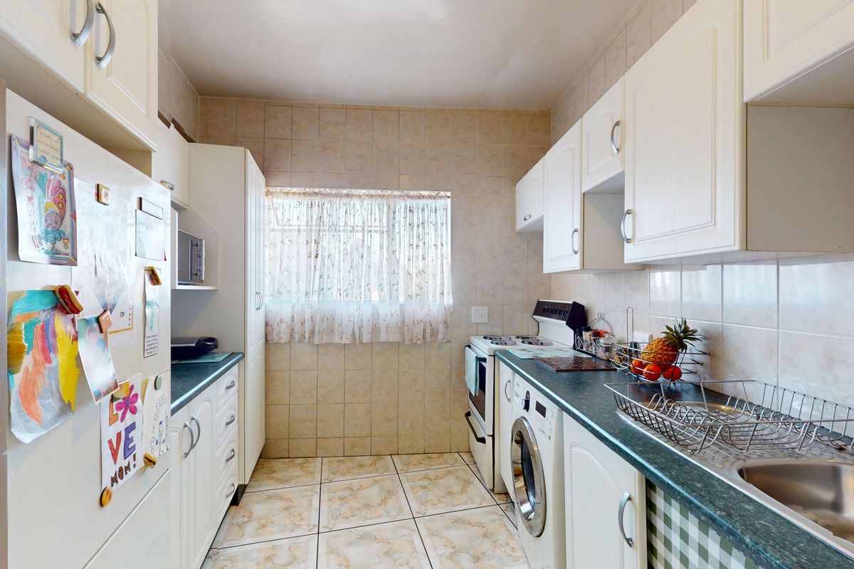A functional galley-style kitchen featuring white cabinetry, tiled backsplash, laminate countertops, and integrated laundry facilities with a window for natural light.