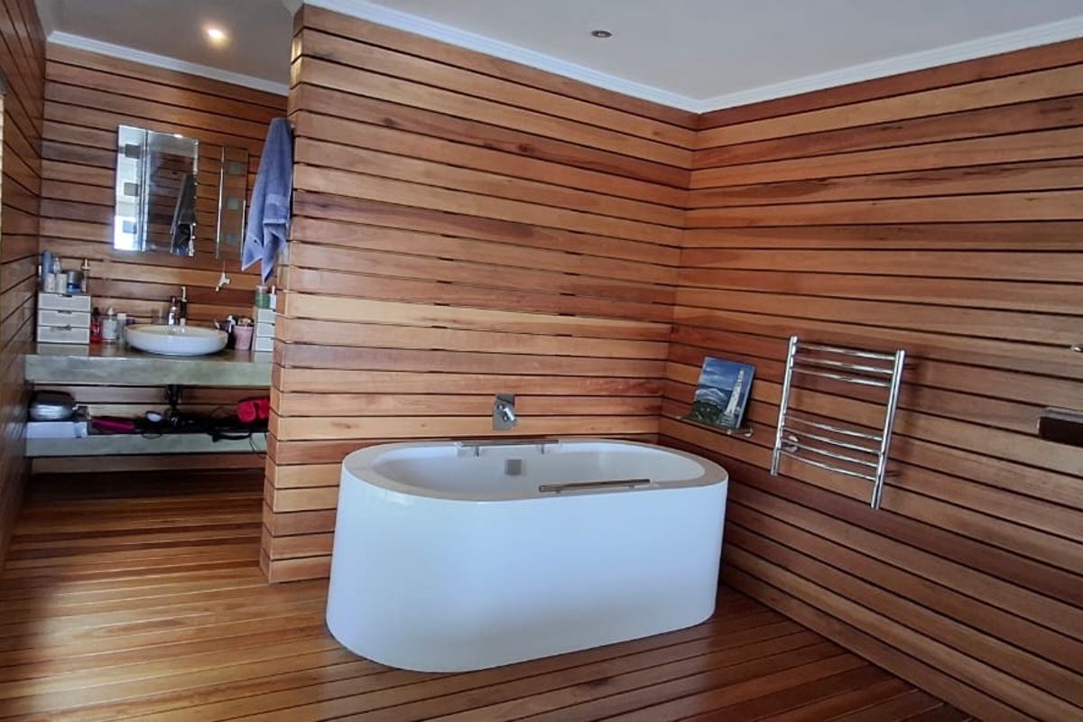 Modern bathroom featuring extensive timber wall cladding and flooring, a sleek freestanding bathtub, concrete vanity top with vessel sink, and a heated towel rail.