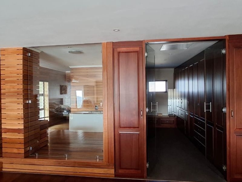 Spacious bedroom area featuring extensive timber wall paneling, custom built-in cabinetry, and a modern glass-enclosed ensuite section with timber flooring.