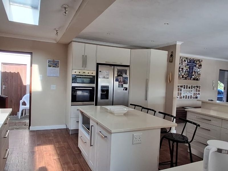 Spacious open-plan kitchen featuring a central island, modern built-in appliances, stone countertops, and a skylight, seamlessly flowing into the adjacent living area.