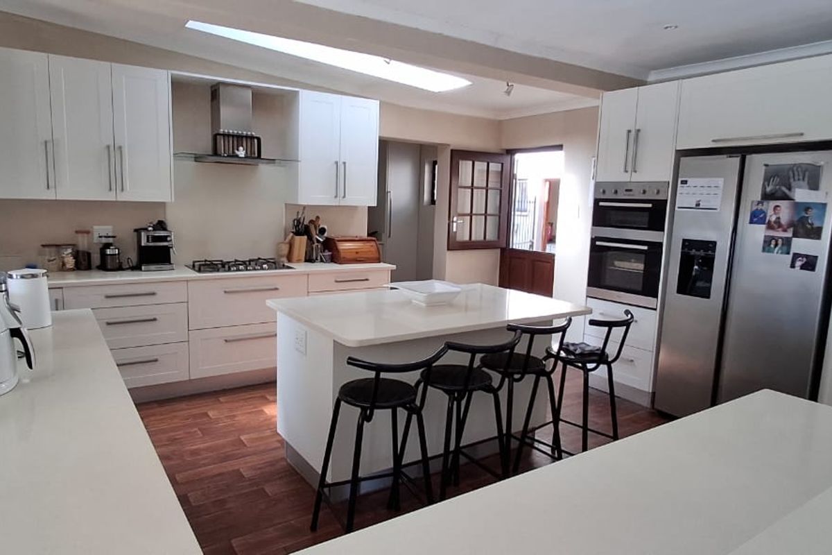 Modern kitchen featuring white cabinetry, stone countertops, a central island with seating, and integrated appliances including a gas hob and double oven.