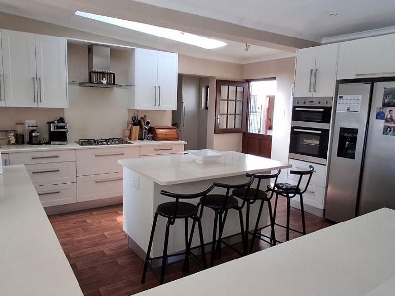 Modern kitchen featuring white cabinetry, stone countertops, a central island with seating, and integrated appliances including a gas hob and double oven.