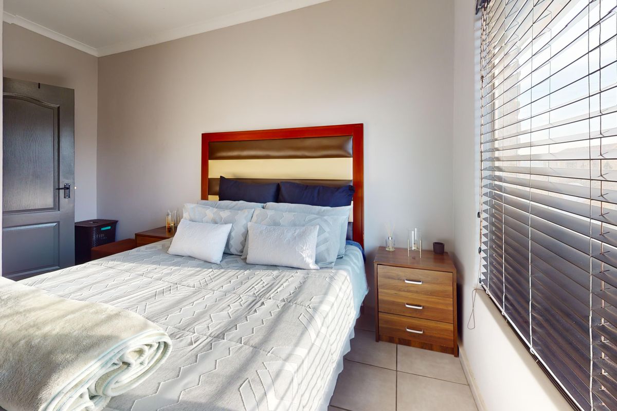 A well-maintained bedroom featuring tiled flooring, neutral wall finishes, and venetian blinds providing natural light control.