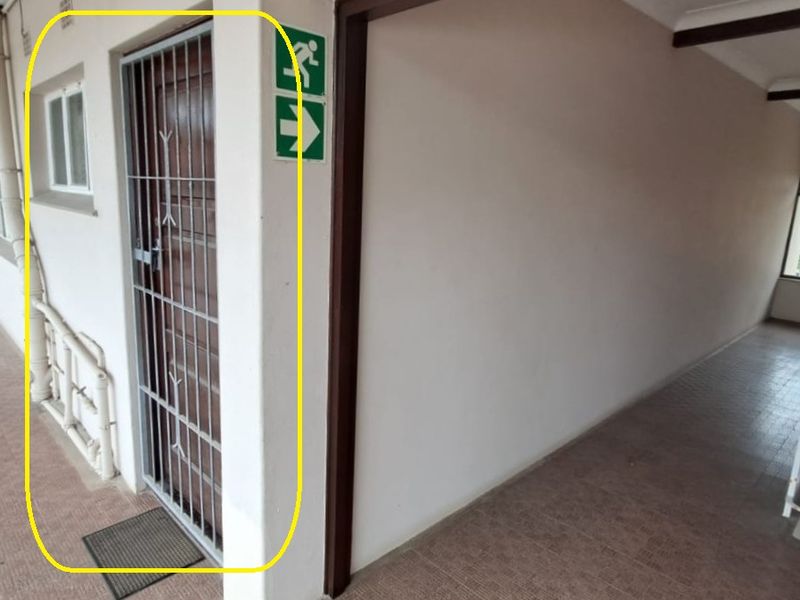 An exterior apartment hallway featuring tiled flooring, a security gate at the entrance, and emergency exit signage.