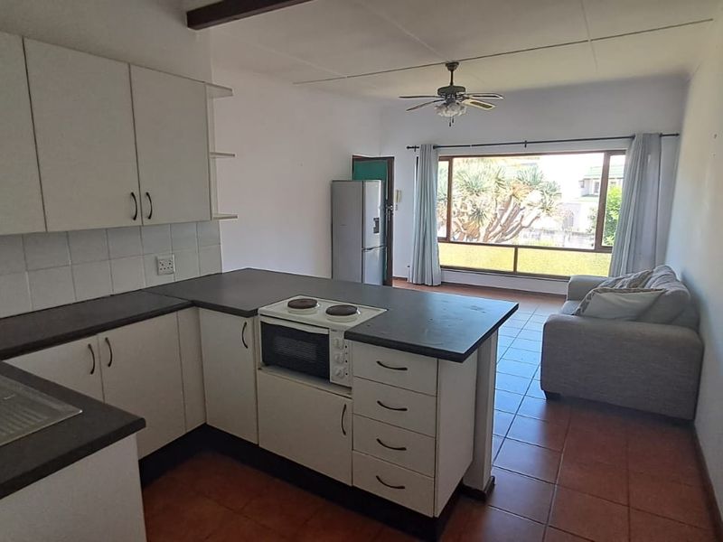 Open-plan kitchen and living area featuring tiled flooring, built-in cabinetry with integrated oven and hob, and large windows providing natural light.