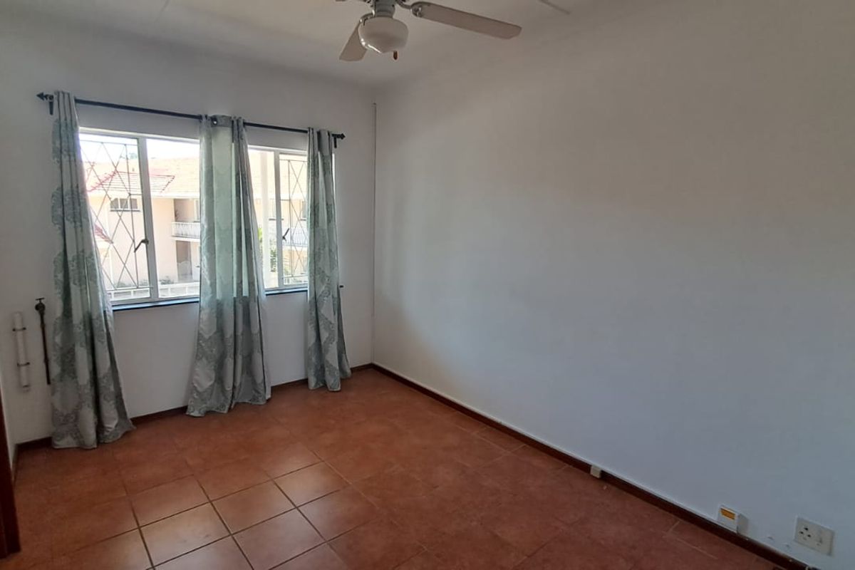 A bright, empty bedroom featuring tiled flooring, a ceiling fan, and security bars on the windows, offering a clean canvas for personalization.