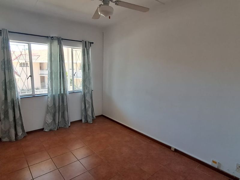 A bright, empty bedroom featuring tiled flooring, a ceiling fan, and security bars on the windows, offering a clean canvas for personalization.