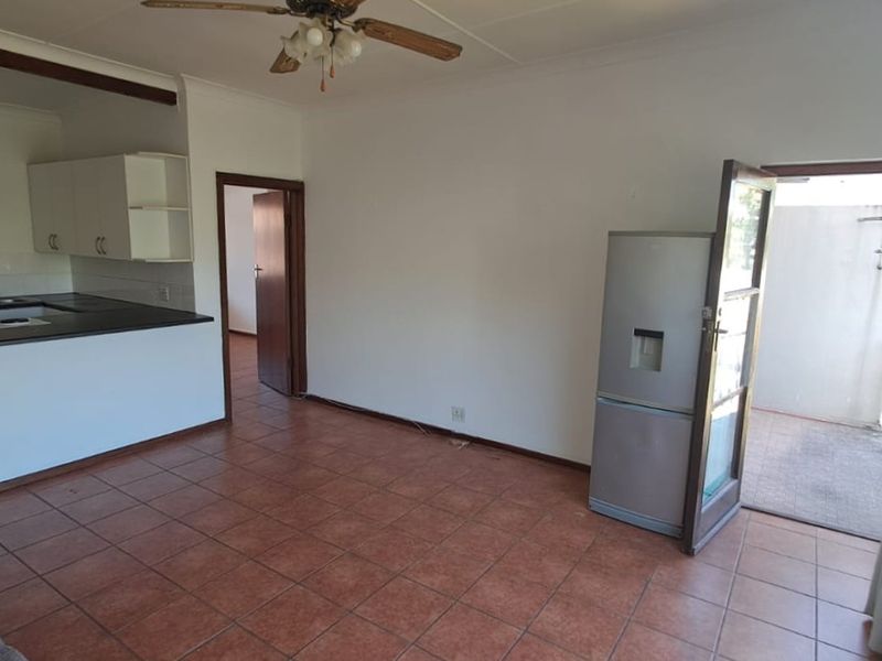 Open-plan living area featuring tiled flooring, a ceiling fan, and an adjoining kitchen with built-in cabinetry and hob, leading to an outdoor patio area.