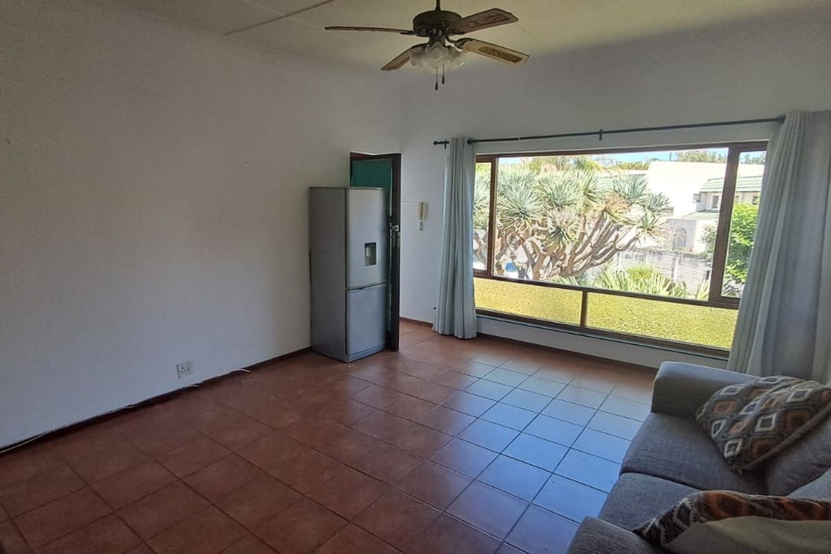 A living room featuring tiled flooring, a ceiling fan, and a large window providing natural light and garden views.