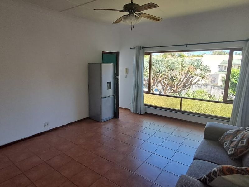 A living room featuring tiled flooring, a ceiling fan, and a large window providing natural light and garden views.