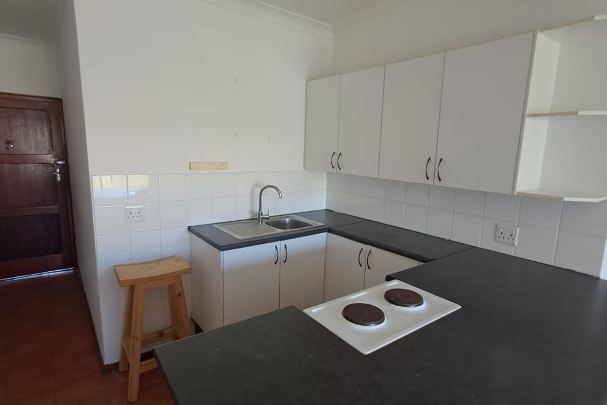 A functional kitchen featuring white cabinetry, dark laminate countertops, a stainless steel sink, and a built-in electric hob with a tiled backsplash.