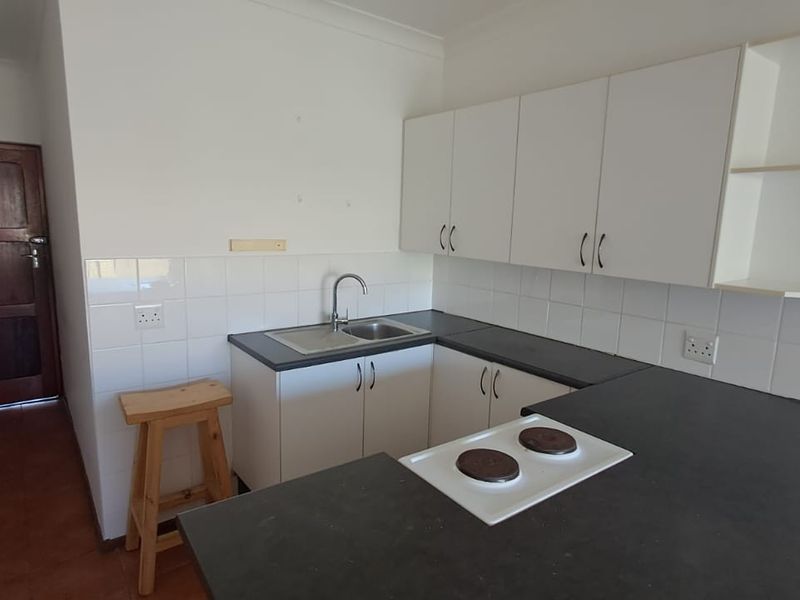 A functional kitchen featuring white cabinetry, dark laminate countertops, a stainless steel sink, and a built-in electric hob with a tiled backsplash.
