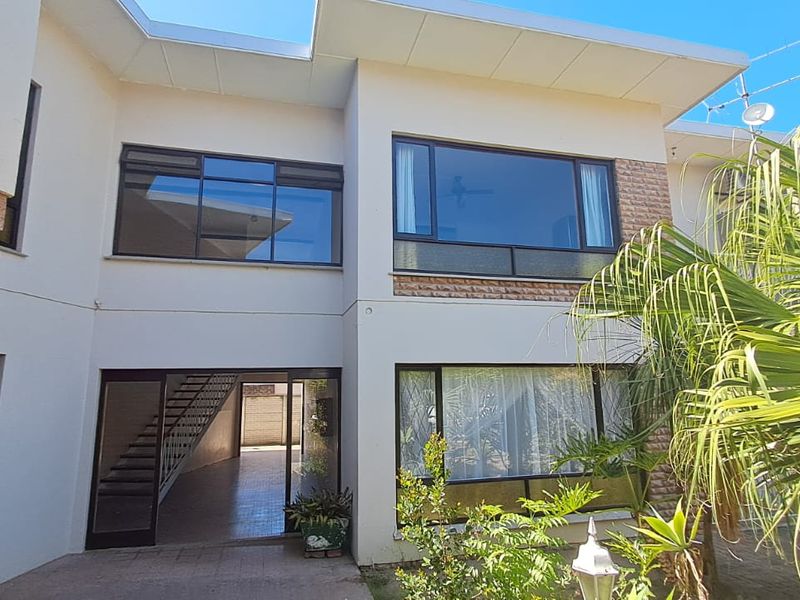 Rear elevation of the apartment building featuring large windows, stone cladding accents, and a ground-level patio area with access to an internal staircase.