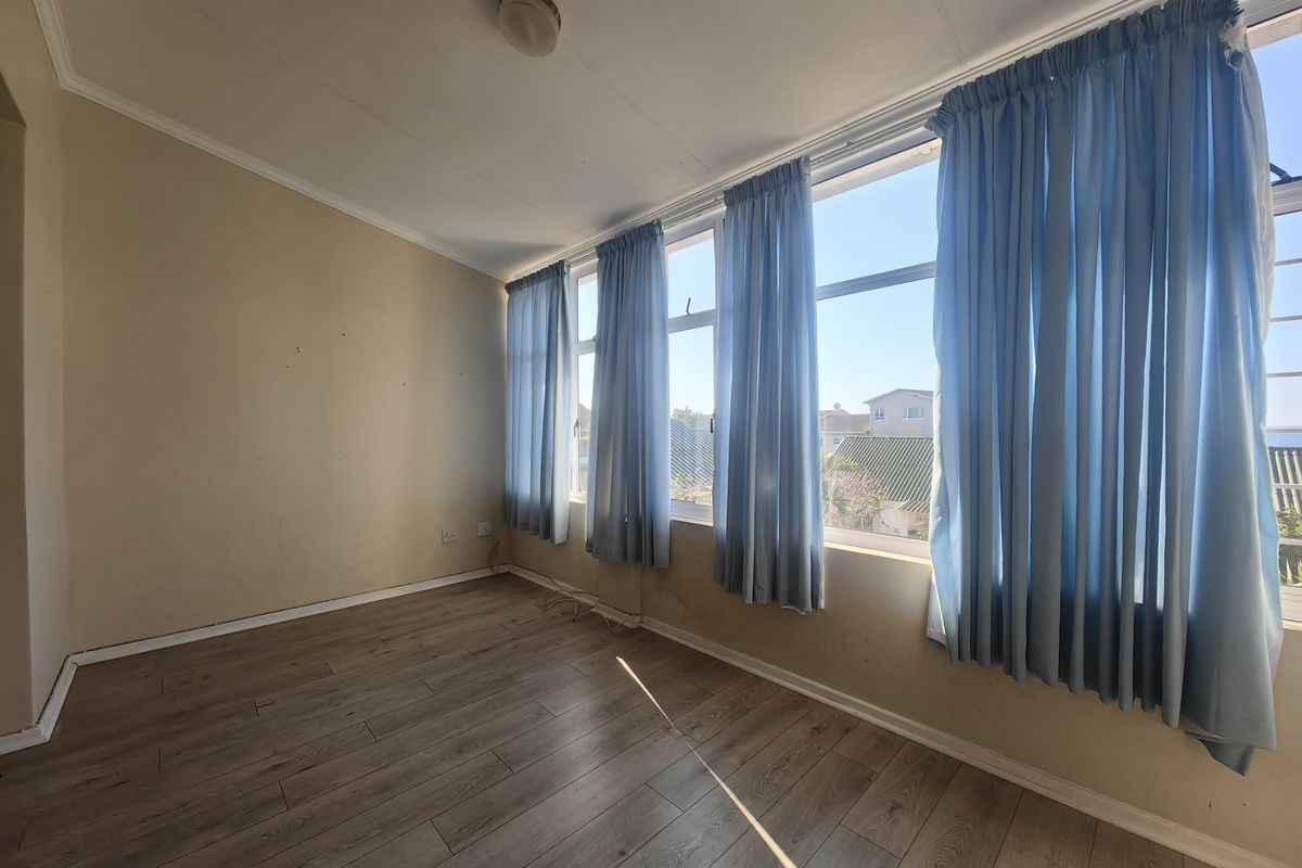 An empty bedroom featuring laminate flooring and large windows with natural light, requiring minor wall repairs and cosmetic updates.