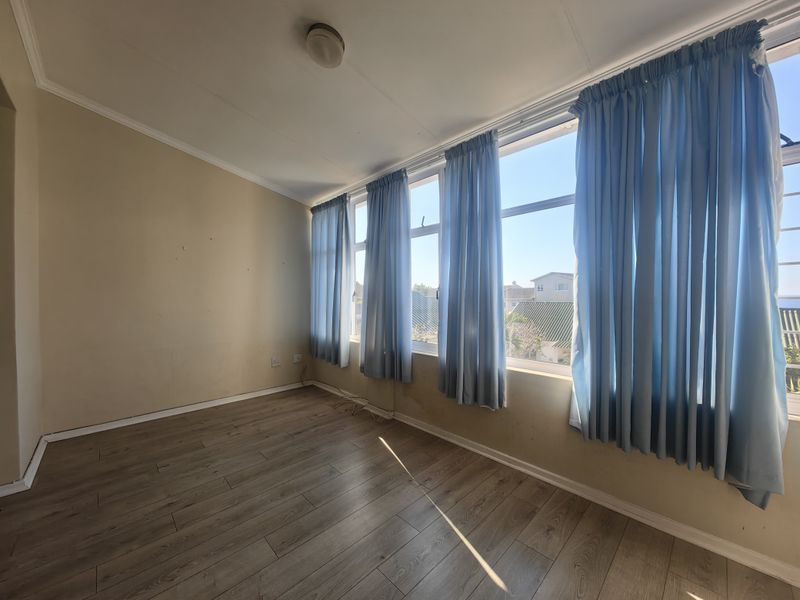 An empty bedroom featuring laminate flooring and large windows with natural light, requiring minor wall repairs and cosmetic updates.